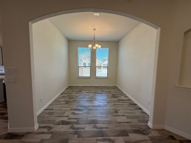 unfurnished dining area featuring arched walkways, a chandelier, baseboards, and wood finished floors