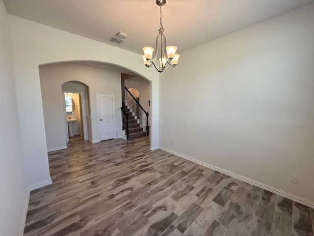 unfurnished room with baseboards, stairway, an inviting chandelier, wood finished floors, and arched walkways