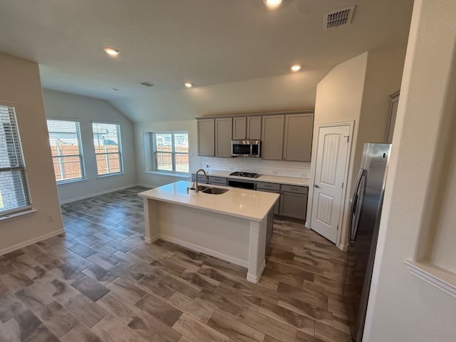 kitchen featuring visible vents, vaulted ceiling, gray cabinets, stainless steel appliances, and a sink