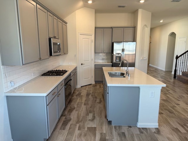 kitchen featuring visible vents, arched walkways, gray cabinetry, a sink, and appliances with stainless steel finishes