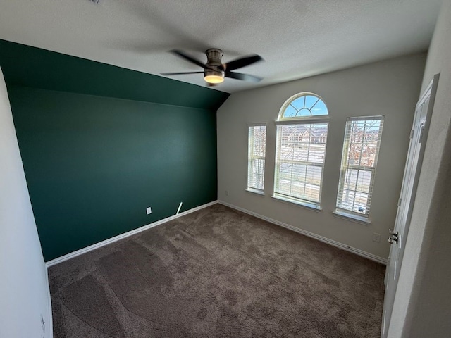 unfurnished room with baseboards, dark carpet, lofted ceiling, a textured ceiling, and a ceiling fan