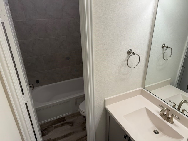 full bath with toilet, wood finished floors, shower / bath combination, vanity, and a textured wall