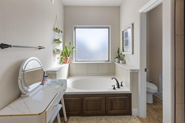 bathroom featuring toilet, a garden tub, and wood finished floors