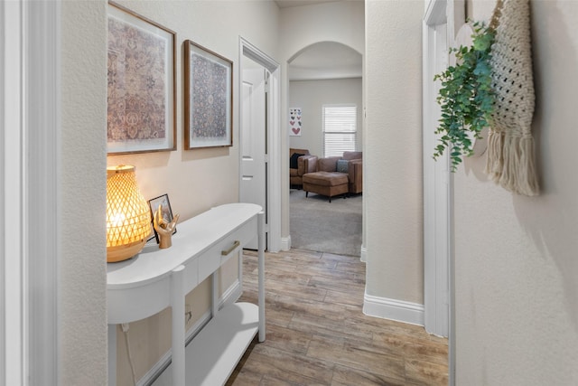 hallway with baseboards, arched walkways, and wood finished floors