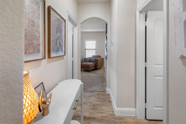 corridor featuring baseboards, arched walkways, wood finished floors, and a textured wall