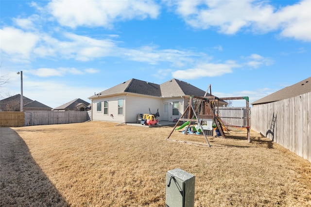 rear view of property featuring a patio area, a playground, a lawn, and a fenced backyard