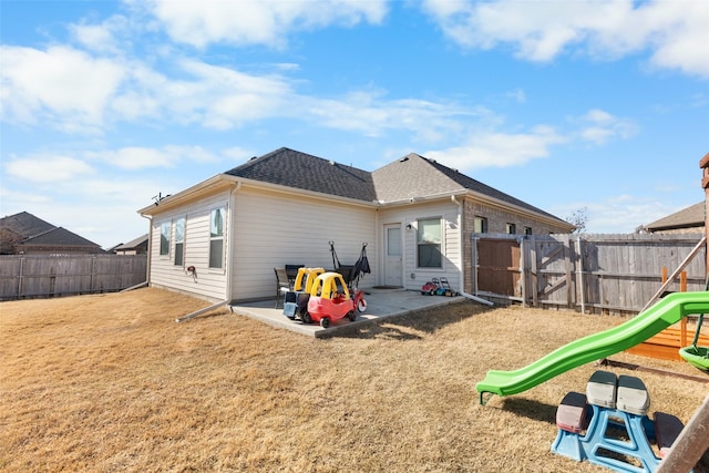 back of house with roof with shingles, a yard, a fenced backyard, a playground, and a patio area