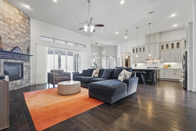 living room featuring dark wood-type flooring, a fireplace, visible vents, and a towering ceiling