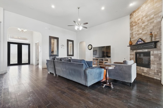 living room with a tiled fireplace, ceiling fan with notable chandelier, wood finished floors, arched walkways, and a high ceiling