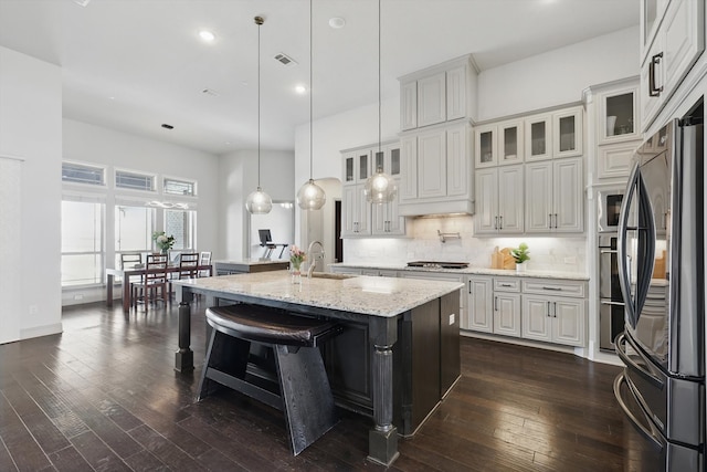 kitchen with a center island with sink, dark wood-style floors, stainless steel appliances, a breakfast bar area, and decorative backsplash