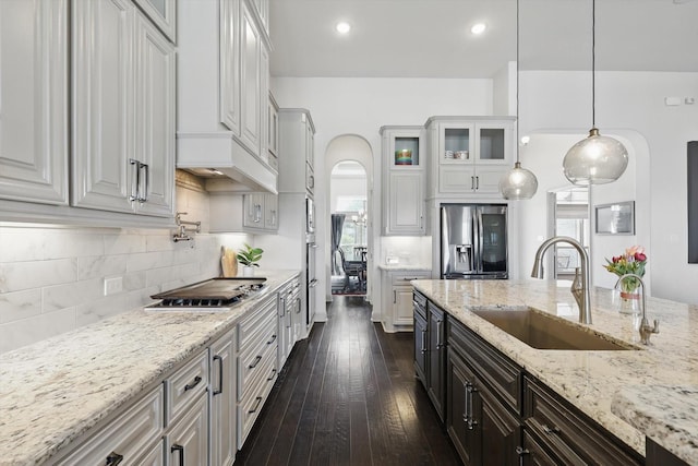 kitchen with glass insert cabinets, dark wood-type flooring, arched walkways, stainless steel appliances, and a sink