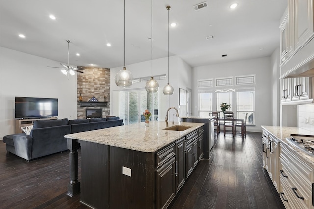 kitchen with visible vents, dark wood-style flooring, a stone fireplace, and a sink