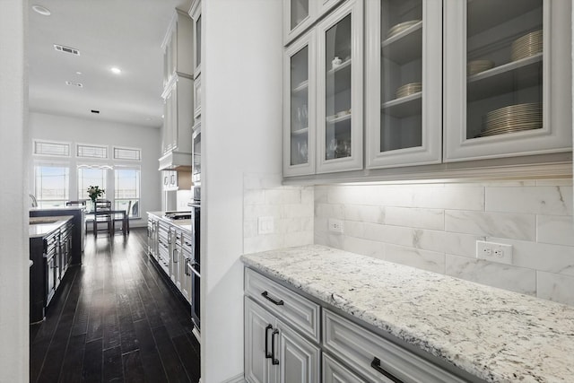 kitchen with visible vents, glass insert cabinets, light stone countertops, dark wood finished floors, and decorative backsplash