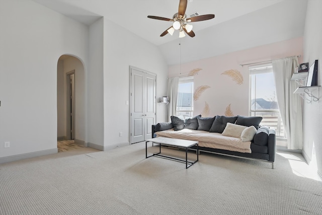 living room with a wealth of natural light, arched walkways, light colored carpet, and a ceiling fan