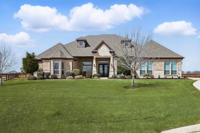 french country inspired facade with brick siding, french doors, a front yard, and roof with shingles