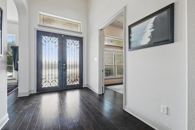 foyer entrance featuring dark wood finished floors, arched walkways, baseboards, and a textured wall