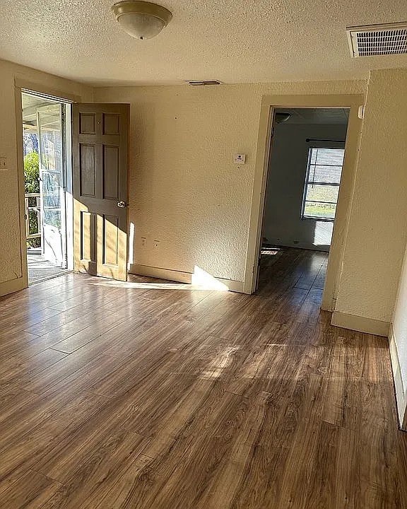 empty room with dark wood finished floors, visible vents, a healthy amount of sunlight, and a textured wall