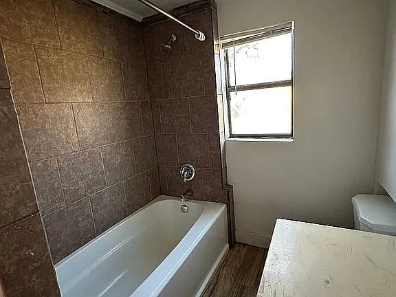 bathroom with toilet, wood finished floors, and shower / washtub combination