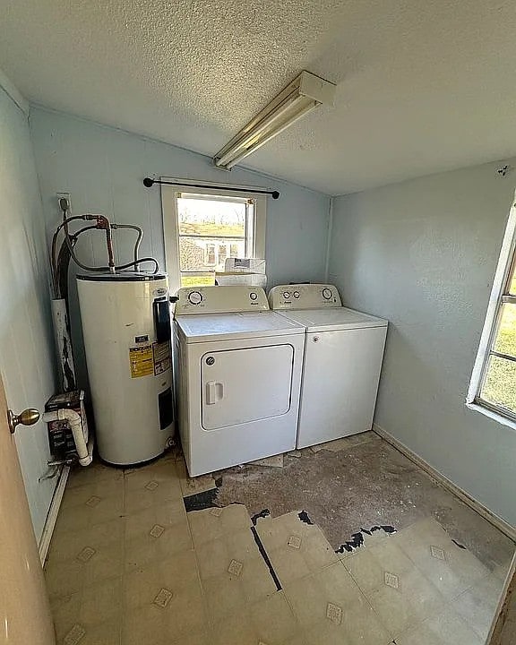 clothes washing area featuring laundry area, plenty of natural light, electric water heater, and separate washer and dryer