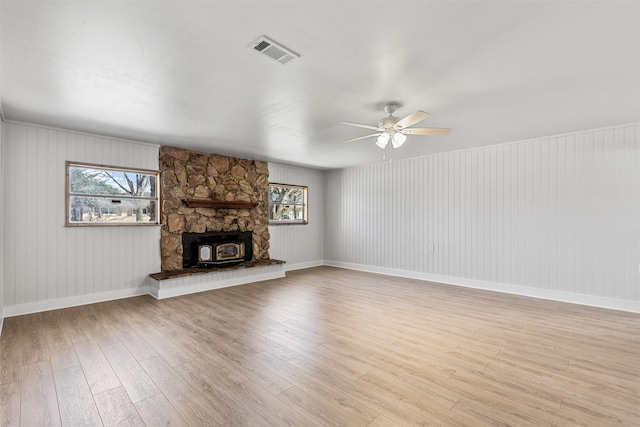 unfurnished living room with visible vents, baseboards, a wood stove, ceiling fan, and light wood-style floors