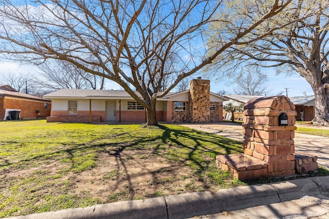 view of front of home with a front yard, concrete driveway, brick siding, and a chimney