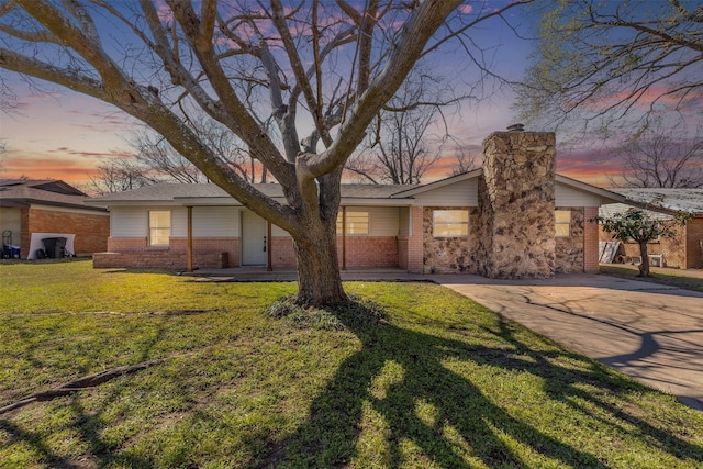 mid-century home featuring a yard, brick siding, driveway, and a chimney