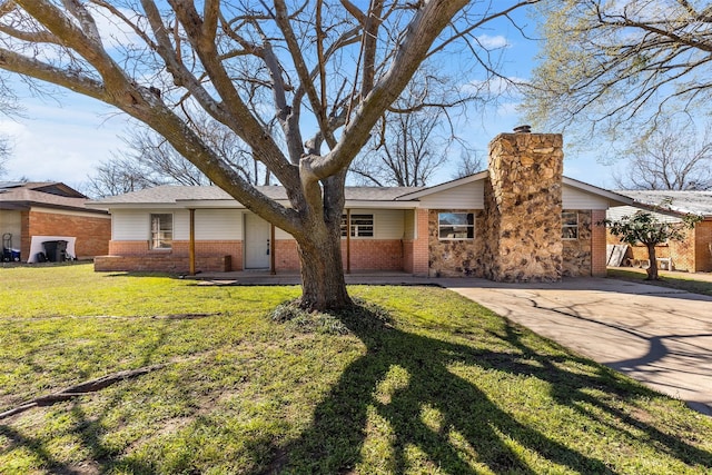 view of front of house featuring driveway, brick siding, a chimney, and a front yard