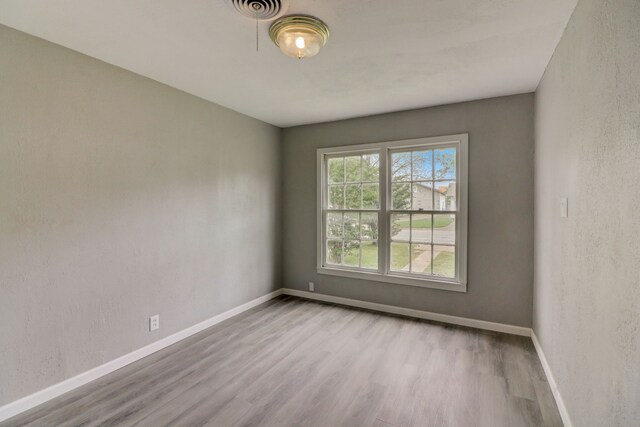 empty room featuring a textured wall, visible vents, baseboards, and wood finished floors