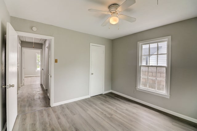 unfurnished bedroom featuring baseboards, light wood-style floors, attic access, and ceiling fan