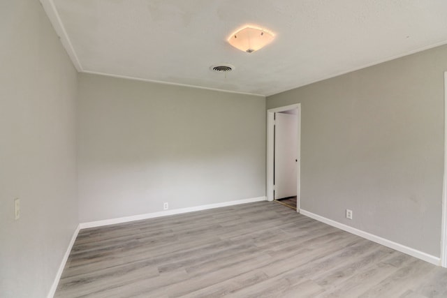 unfurnished room with light wood-type flooring, visible vents, baseboards, and ornamental molding