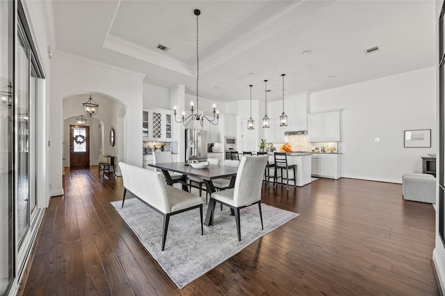 dining room with visible vents, dark wood finished floors, a tray ceiling, an inviting chandelier, and arched walkways