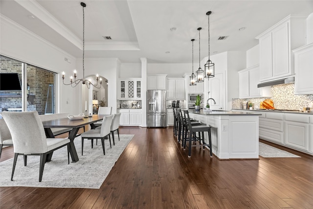 dining space with dark wood-style floors, visible vents, ornamental molding, a raised ceiling, and a notable chandelier