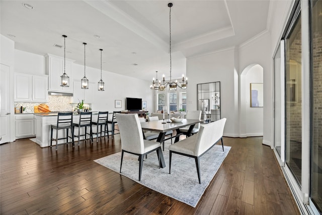 dining room with a tray ceiling, arched walkways, dark wood-style floors, and ornamental molding