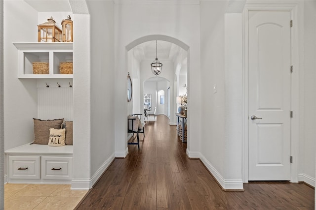 hallway with wood finished floors, arched walkways, and baseboards