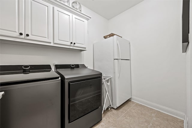 laundry area featuring light tile patterned floors, baseboards, cabinet space, and washer and clothes dryer