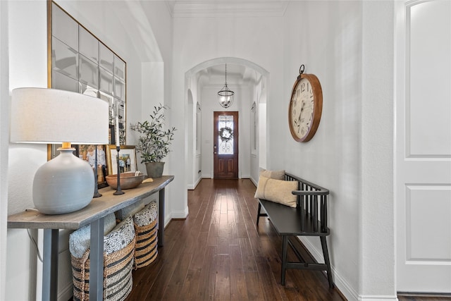 foyer entrance featuring dark wood-type flooring, baseboards, arched walkways, and ornamental molding