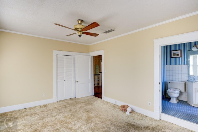 unfurnished bedroom with ensuite bath, crown molding, carpet, and a closet