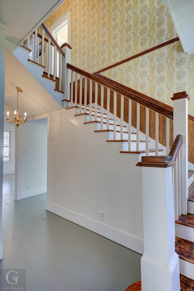 stairway featuring baseboards, a notable chandelier, wood finished floors, and wallpapered walls