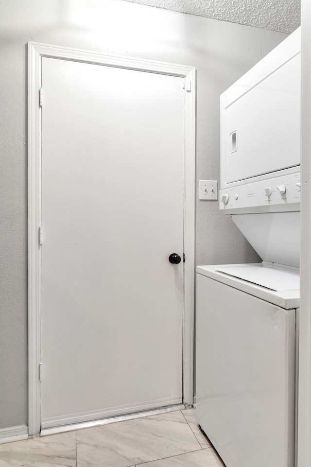 clothes washing area with stacked washer / drying machine, marble finish floor, and laundry area