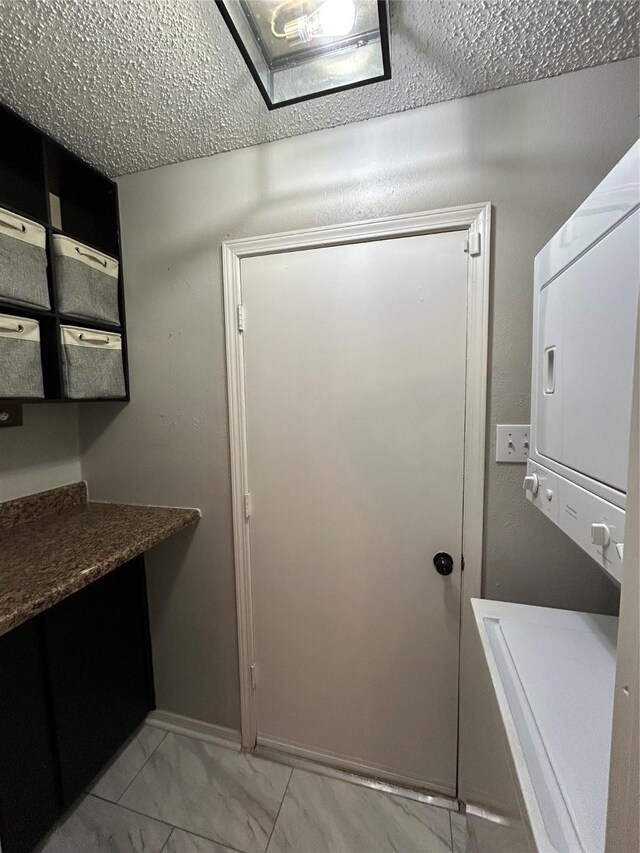 laundry room featuring laundry area, marble finish floor, a textured ceiling, and stacked washer / drying machine