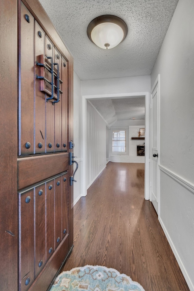 corridor with dark wood finished floors, baseboards, and a textured ceiling