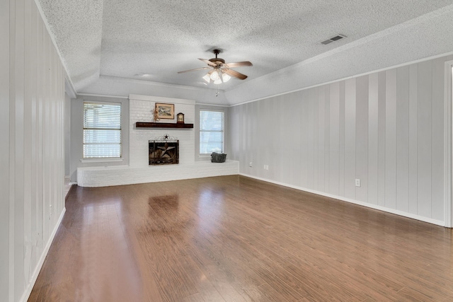 unfurnished living room with a ceiling fan, visible vents, dark wood-type flooring, a textured ceiling, and a brick fireplace