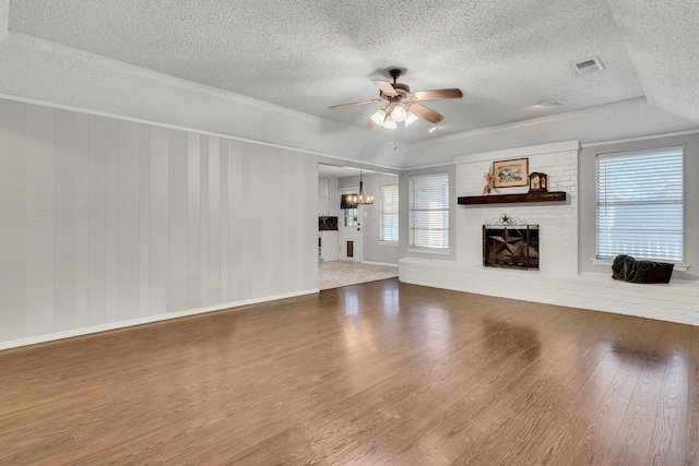 unfurnished living room featuring a wealth of natural light, a brick fireplace, wood finished floors, and ceiling fan with notable chandelier