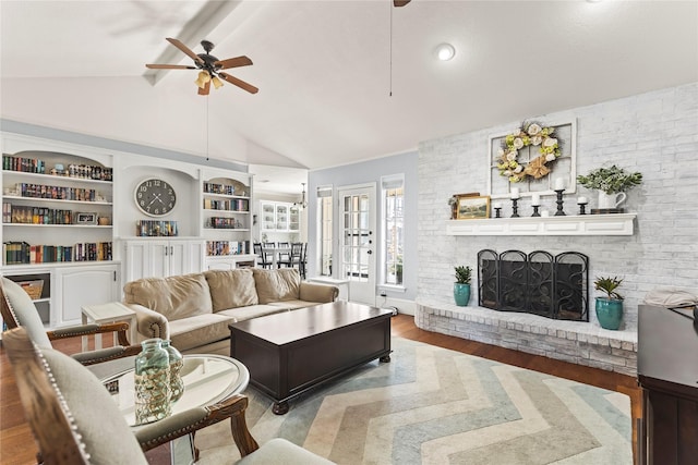 living room featuring a ceiling fan, lofted ceiling with beams, built in features, wood finished floors, and a brick fireplace