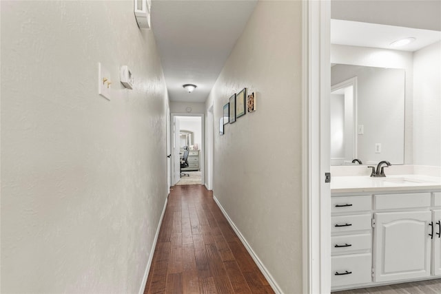 hallway featuring dark wood-style floors, baseboards, a textured wall, and a sink