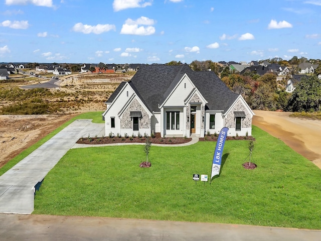 view of front of house with stone siding, a shingled roof, and a front yard