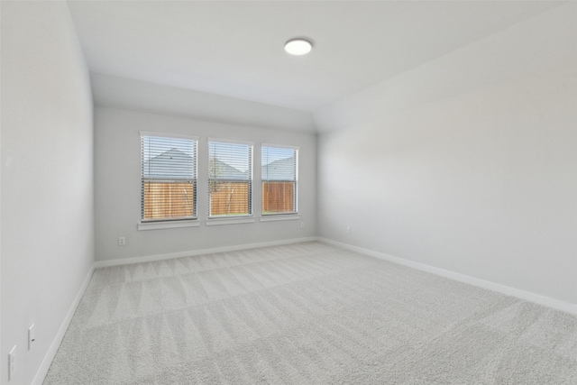 spare room with light carpet, baseboards, and vaulted ceiling