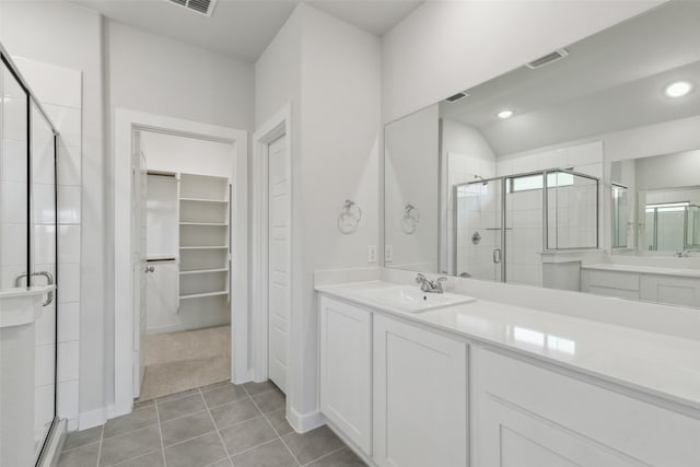 full bathroom featuring tile patterned flooring, visible vents, a walk in closet, a stall shower, and vanity