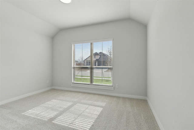 carpeted empty room featuring baseboards and vaulted ceiling