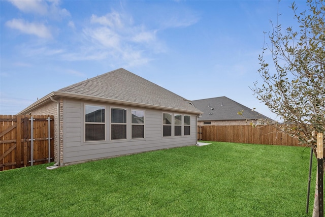 back of house with a fenced backyard, a shingled roof, a yard, and brick siding